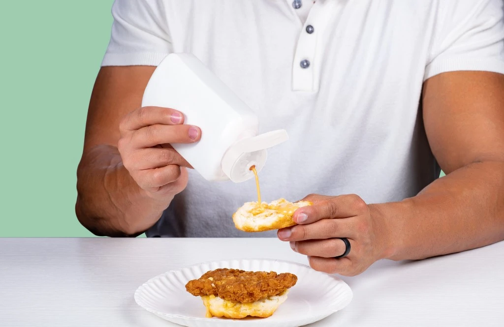 Man squeezing chick fil a sauce onto a chicken sandwich
