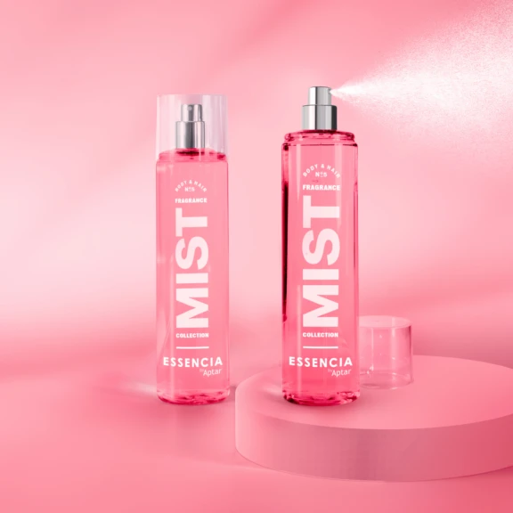 Two pink bottles labeled Fragrance MIST from the Essencia Collection, featuring an elegant fragrance pump, are displayed on a pink surface. One bottle has a cap on, while the other sprays a fine mist against shades of pink in the background.