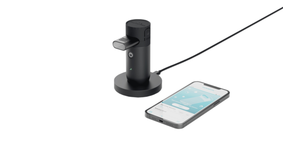 Black Aptar Kolibri inhaler on charging mount with mouthpiece beside digital data tracking app.
