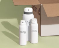 Three white aerosol spray bottles labeled Apollo, Glide, and Vail, an aerosol actuator for large cans, stand in front of an open cardboard box with the Aptar logo.