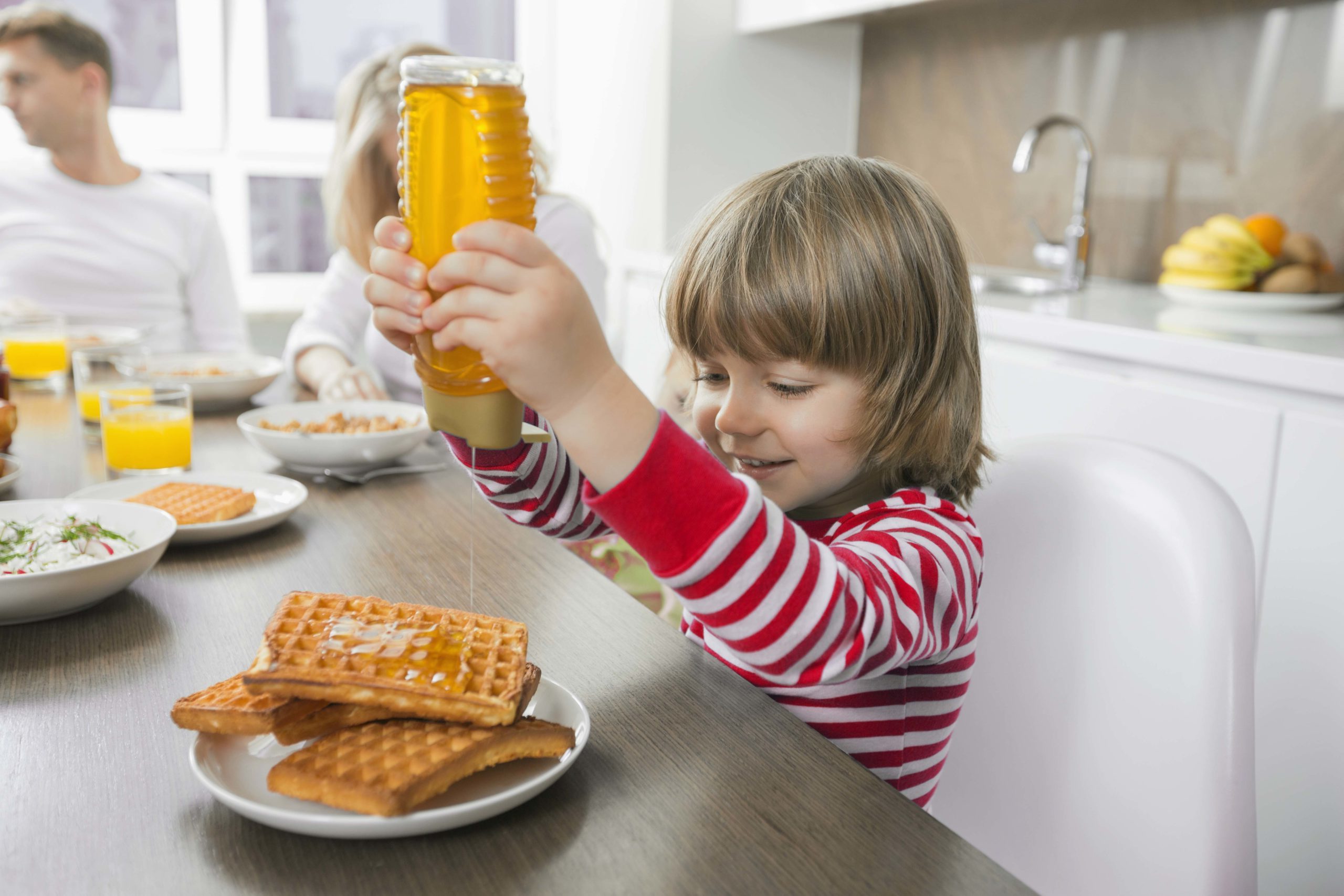 Young child dispensing honey onto waffles in kitchen