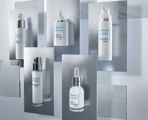 Aptar derma series skincare packaging, including airless, dropper, and dispensing formats, is arranged across layered reflective silver panels with white and metallic finishes against a pale background.