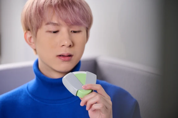 Close up of patient in blue sweater with light colored hair inspecting a green ProHaler inhalation solution with covers open.