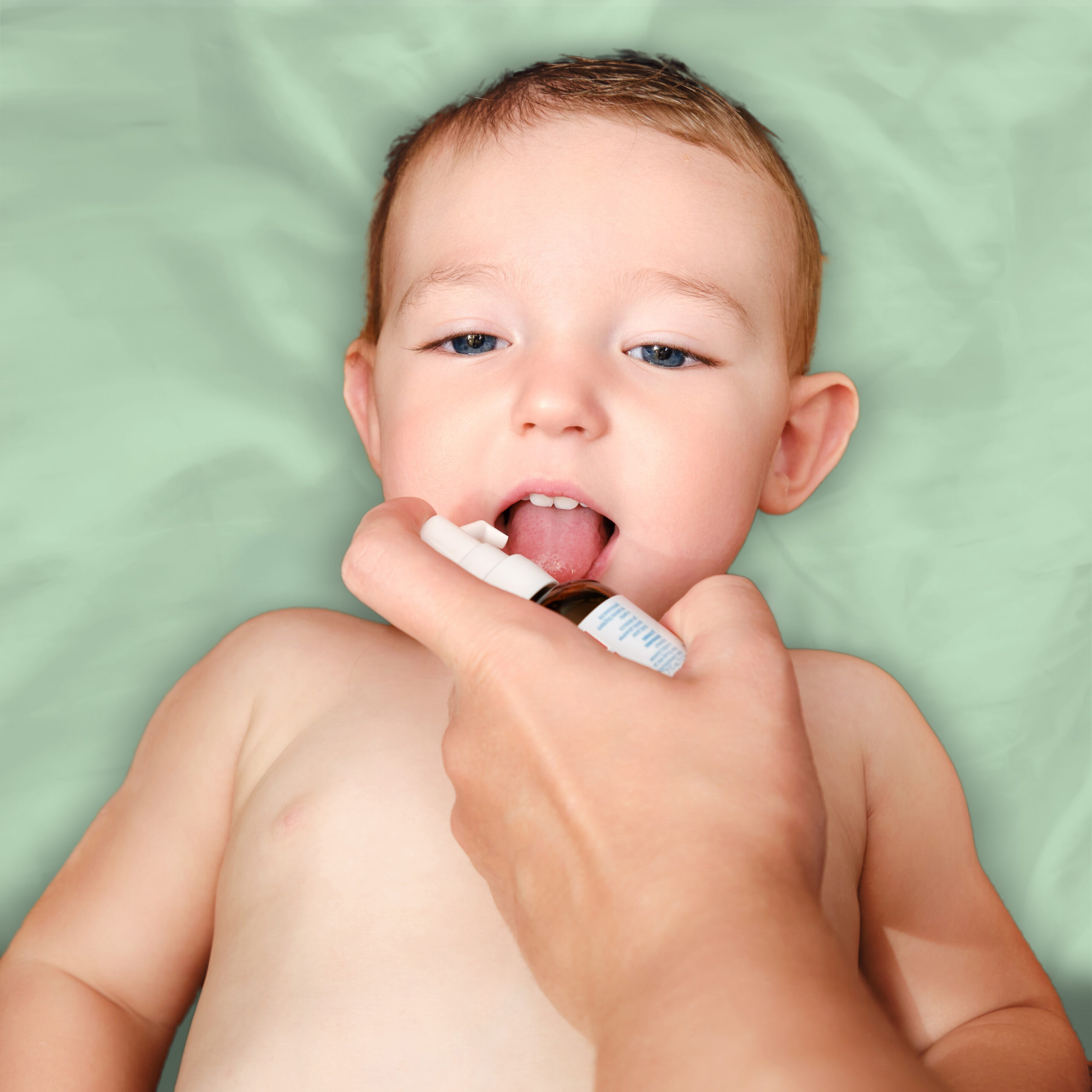 Infant on pillow showing oral gel being dispensed on tongue from oral dispensing system held in parent hand.